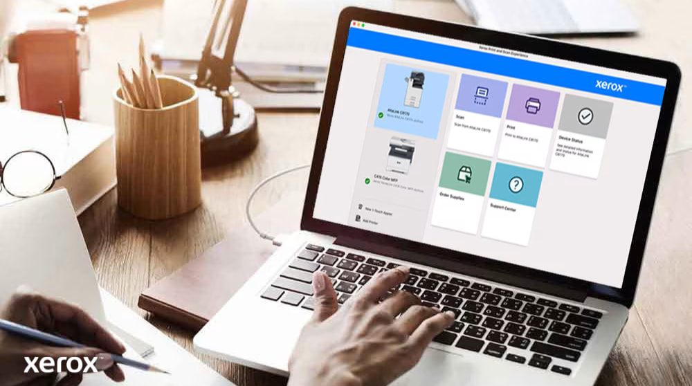 Die Hände einer Person liegen auf einer Laptoptastatur und auf dem Bildschirm wird die Xerox Print and Scan Experience-Benutzeroberfläche mit Optionen wie „Scannen“, „Drucken“, „Gerätestatus“, „Verbrauchsmaterial bestellen“ und „Support Center“ angezeigt, was auf eine benutzerfreundliche Steuerung hindeutet.